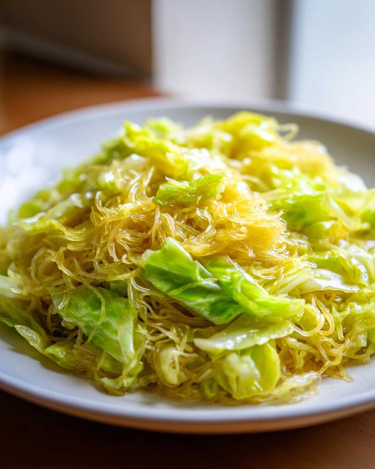 A close-up of a plate piled high with glistening Cabbage Noodle Stir Fry, featuring translucent noodles and bright green cabbage pieces.