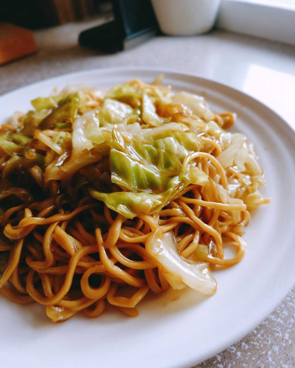 Close-up of a serving of Cabbage Noodle Stir Fry 10 Mins, featuring glossy noodles and bright green cabbage on a white plate.