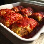 Close-up of baked Cabbage Rolls with Ground Turkey, smothered in rich tomato sauce in a white baking dish.