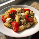 A bright, close-up serving of caprese pasta salad featuring fusilli pasta, cherry tomatoes, and fresh mozzarella balls.