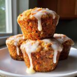 A stack of four moist Carrot Cake Muffins with Tangy Cream Cheese Glaze dripping down the sides.