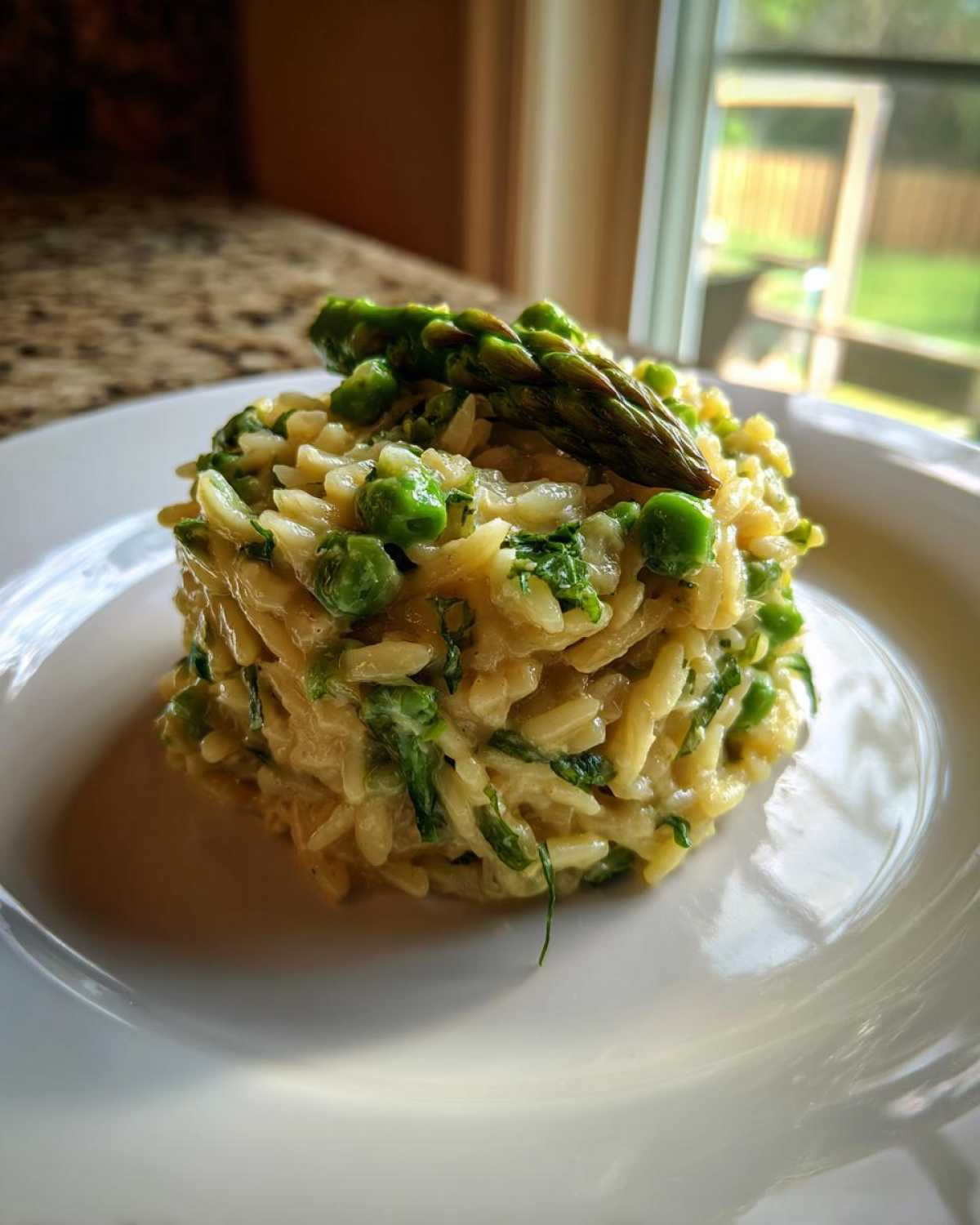 A perfectly molded serving of creamy Cheesy Asparagus Orzotto Recipe topped with fresh asparagus spears and peas.
