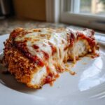 Close-up of a slice of Cheesy Chicken Parmesan showing crispy breading, marinara sauce, and gooey melted mozzarella cheese.
