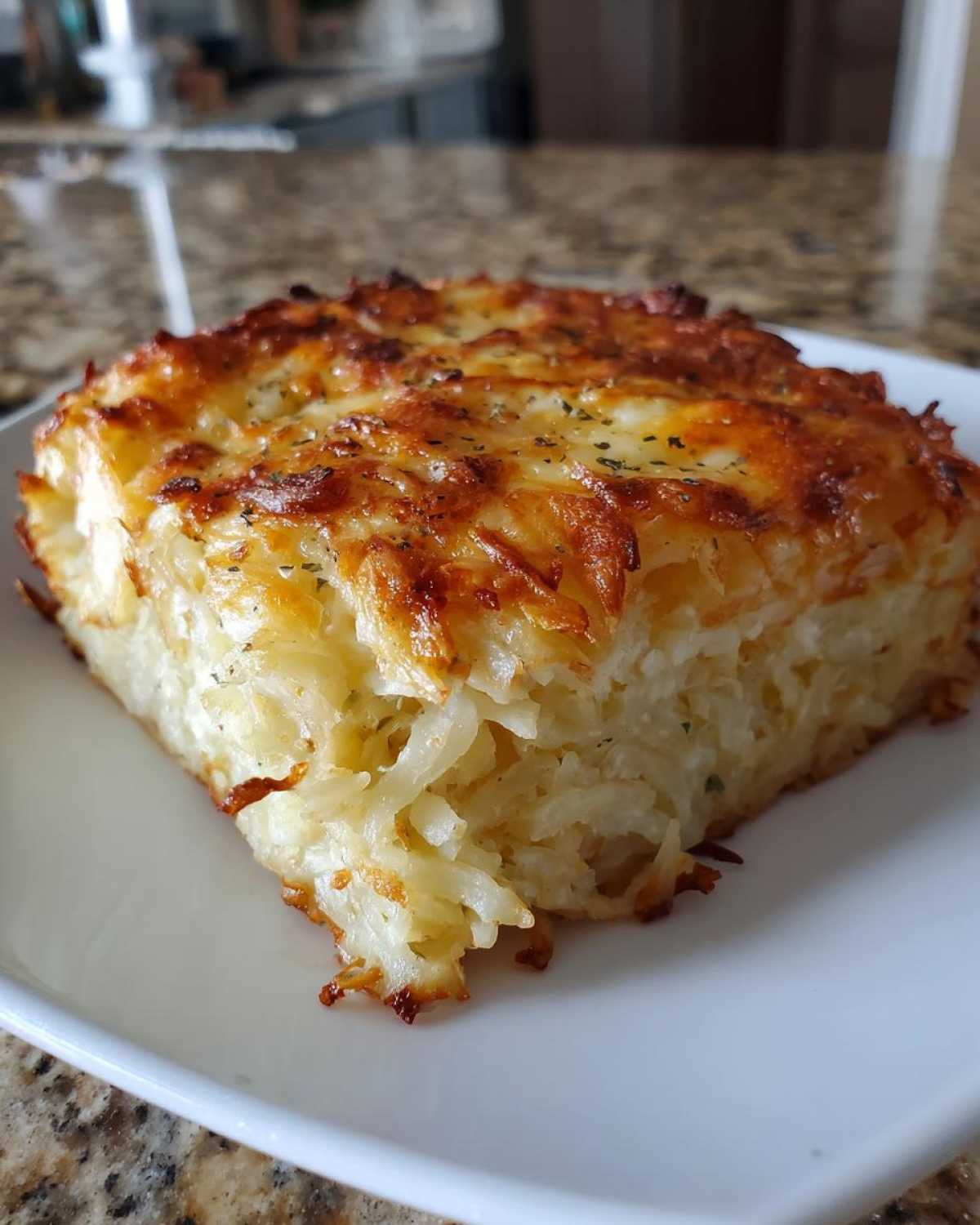 A square slice of creamy, cheesy hashbrown casserole with a golden-brown, baked top.