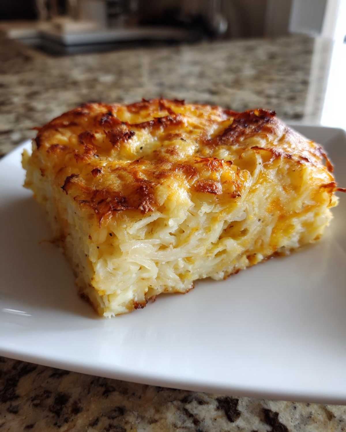 A golden brown slice of cheesy hashbrown casserole with crispy edges served on a white plate.