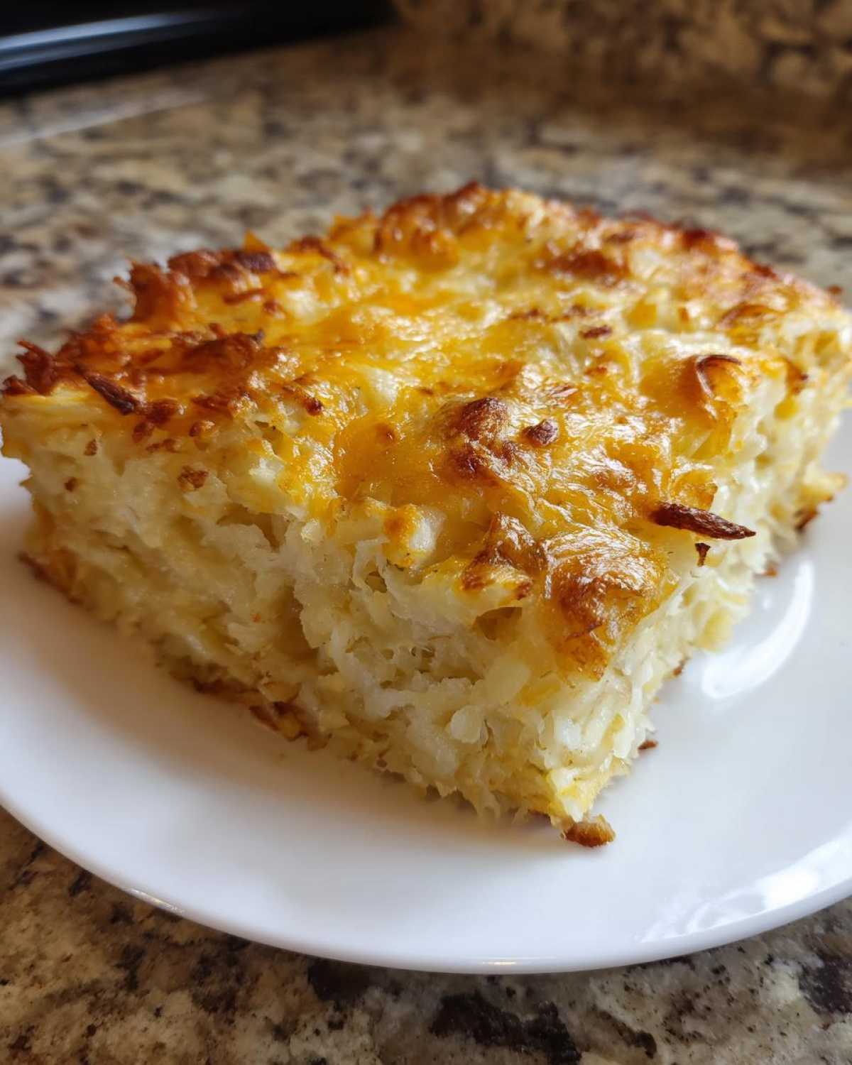 A close-up of a square slice of creamy, cheesy hashbrown casserole with a golden-brown top.