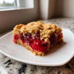A close-up of a square slice of cherry dump cake with a thick, crumbly topping served on a white plate.