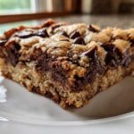 A close-up view of a thick, chewy Chocolate Chip Cookie Bars slice with melted chocolate chunks on a white plate.