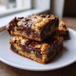 Two thick, chewy Chocolate Chip Cookie Bars stacked on a white plate, showing gooey melted chocolate centers.