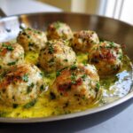 Close-up of golden-brown chicken piccata meatballs simmering in a bright lemon-butter sauce, garnished with parsley.