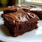 A close-up of a rich, fudgy square of Chocolate Frosted Brownies topped with glossy, swirled chocolate frosting.