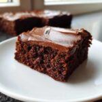 Close-up of a moist, dark square slice of Chocolate Frosted Brownies on a white plate.