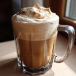 A clear glass mug filled with iced coffee topped generously with thick, whipped Cookie Butter Cold Foam.