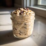A close-up of Cookie Dough Overnight Oats prepared in a glass mason jar, topped with dried fruit.