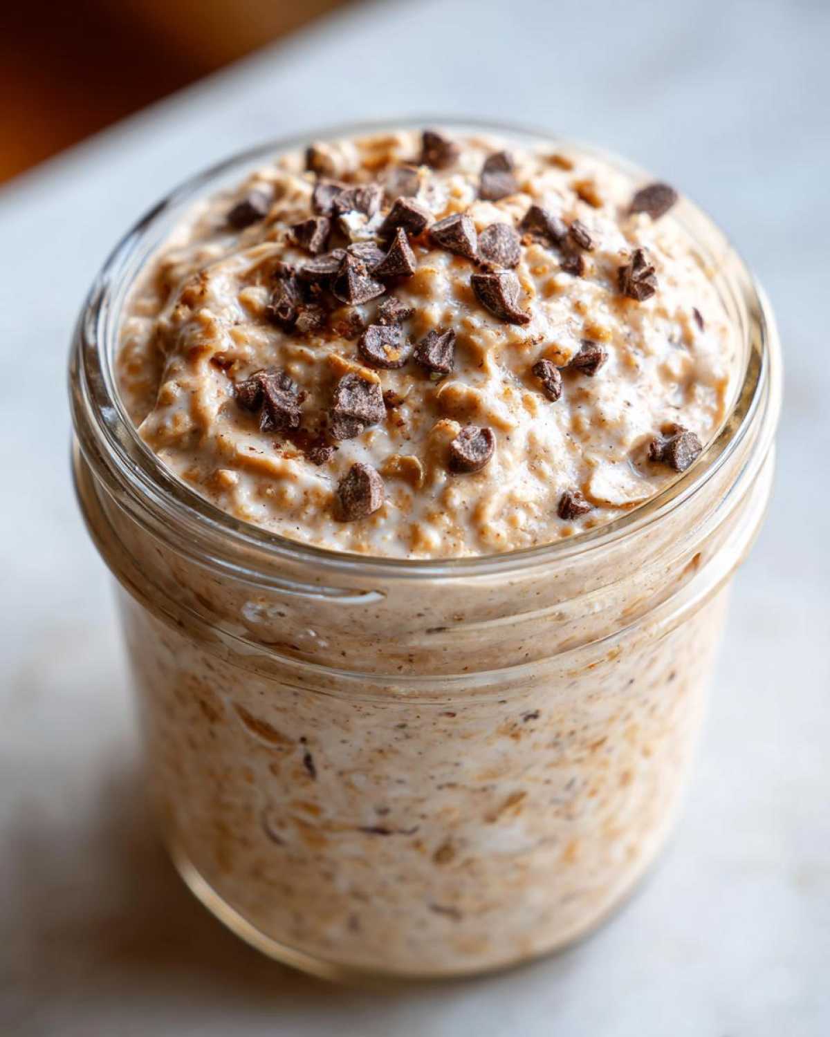A close-up view of creamy Cookie Dough Overnight Oats topped generously with mini chocolate chips in a glass jar.