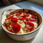A close-up of a baked cottage cheese pizza bowl topped with melted white cheese and crispy pepperoni slices.