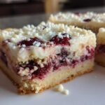 A close-up slice of cranberry bliss bars showing the cake base, tart cranberry filling, and white chocolate frosting with sprinkles.