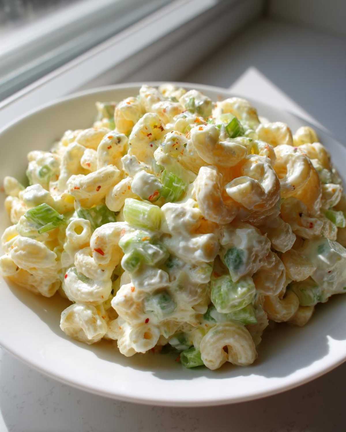 Close-up of creamy Amish macaroni salad with elbow pasta and chopped celery, served in a white bowl.