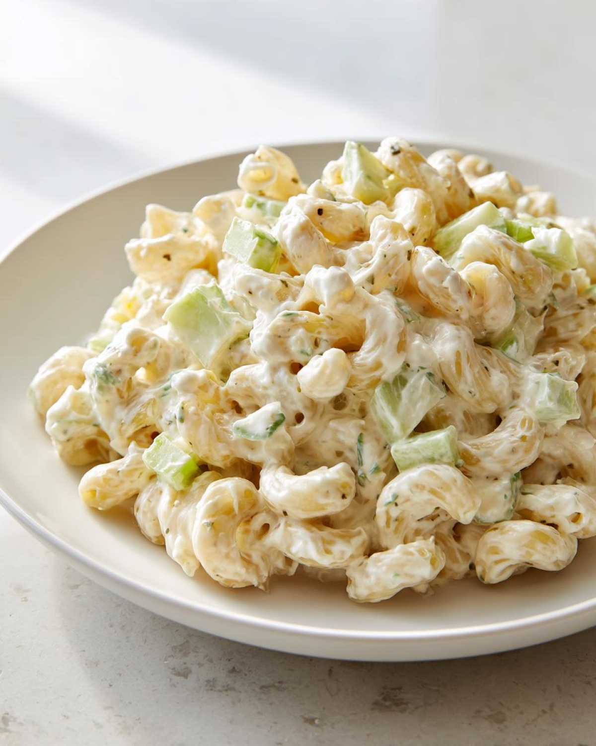 Close-up of a serving of creamy amish macaroni salad featuring elbow macaroni coated in a rich dressing and mixed with chunks of green cucumber.