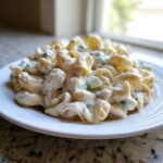 A close-up of creamy Amish macaroni salad featuring elbow macaroni coated in a rich dressing with visible pieces of celery or cucumber.