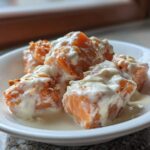 Close-up of crispy, orange Bang Bang Salmon Bites generously drizzled with creamy white sauce in a small white bowl.