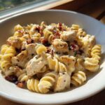 Close-up of creamy chicken bacon ranch pasta with rotini noodles, chunks of chicken, and bacon bits in a white bowl.