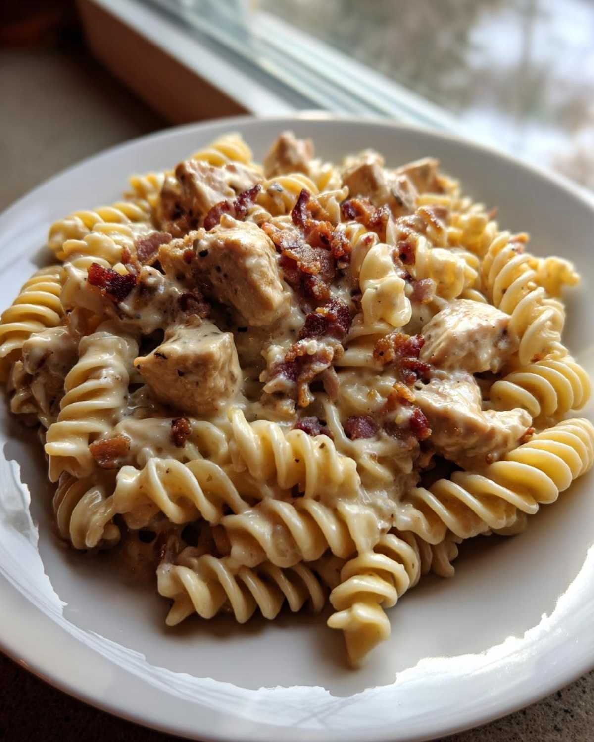 A close-up of creamy chicken bacon ranch pasta made with fusilli noodles, served on a white plate.
