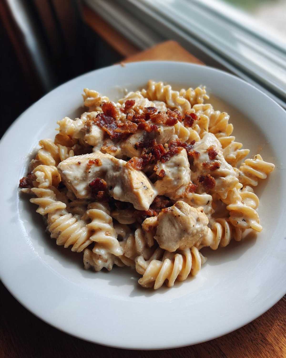 A close-up of creamy chicken bacon ranch pasta made with fusilli noodles, topped with chicken chunks and crispy bacon bits.