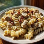 A close-up of creamy chicken bacon ranch pasta made with rotini noodles, chunks of chicken, and bacon bits.
