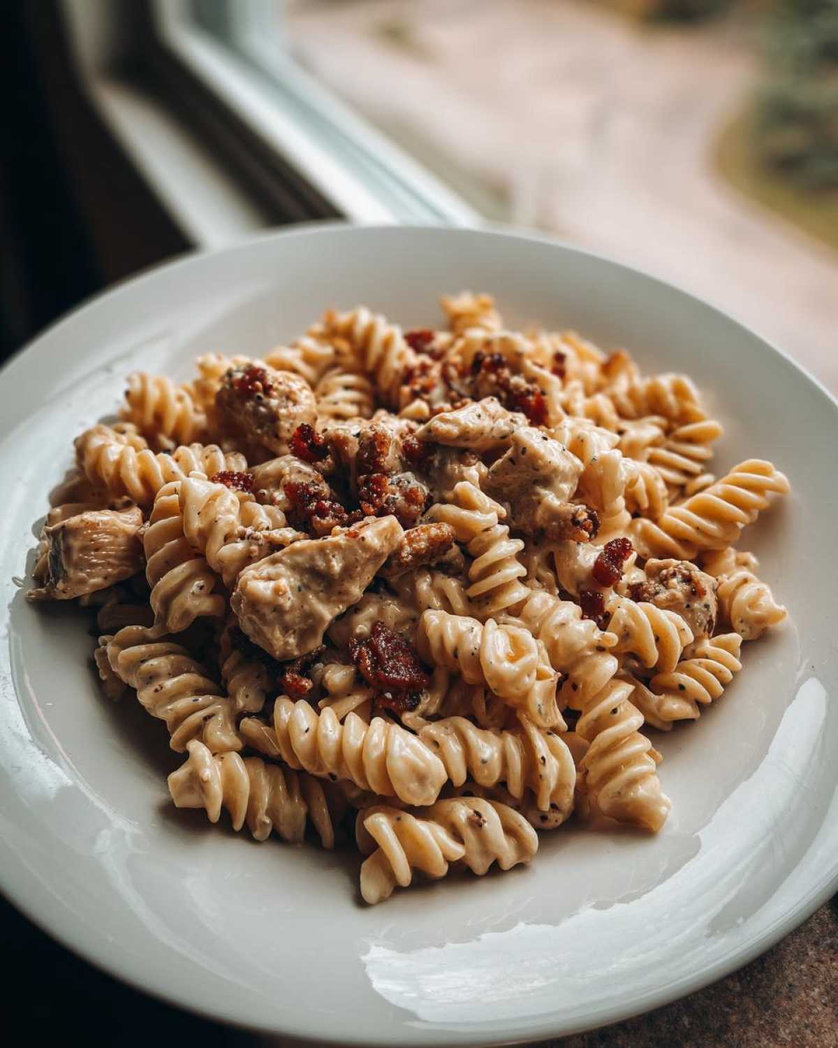 A close-up of creamy chicken bacon ranch pasta made with rotini noodles, served on a white plate.