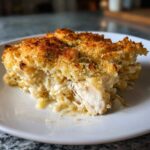 A close-up serving of creamy chicken pasta bake showing shredded chicken breast and a golden, crispy breadcrumb topping.