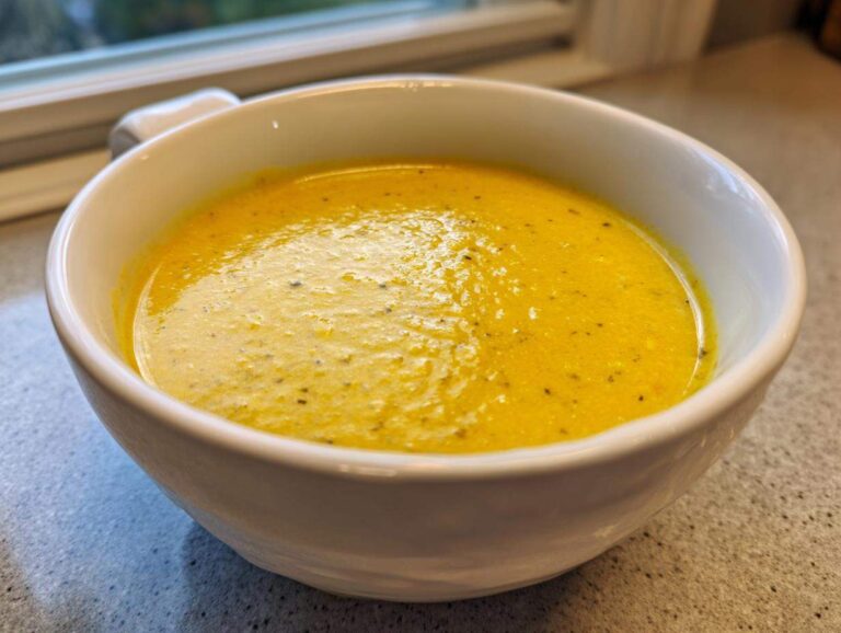 Amazing 30-Minute Creamy Corn Soup Close-up of a white bowl filled with bright yellow, creamy corn soup, lightly seasoned with pepper.