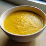 Close-up of a bowl filled with thick, bright yellow creamy corn soup, showing texture and whole corn kernels.