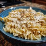 A close-up of rotini pasta coated in creamy cottage cheese alfredo sauce, topped with pepper.