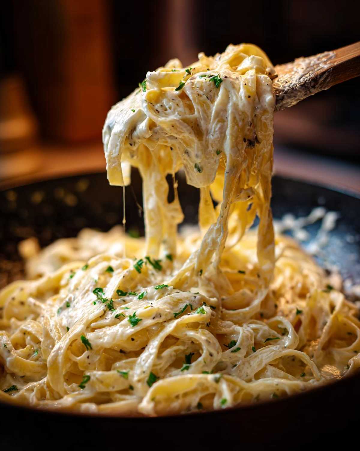 Fettuccine pasta coated in creamy cottage cheese alfredo sauce being lifted by a wooden spoon.