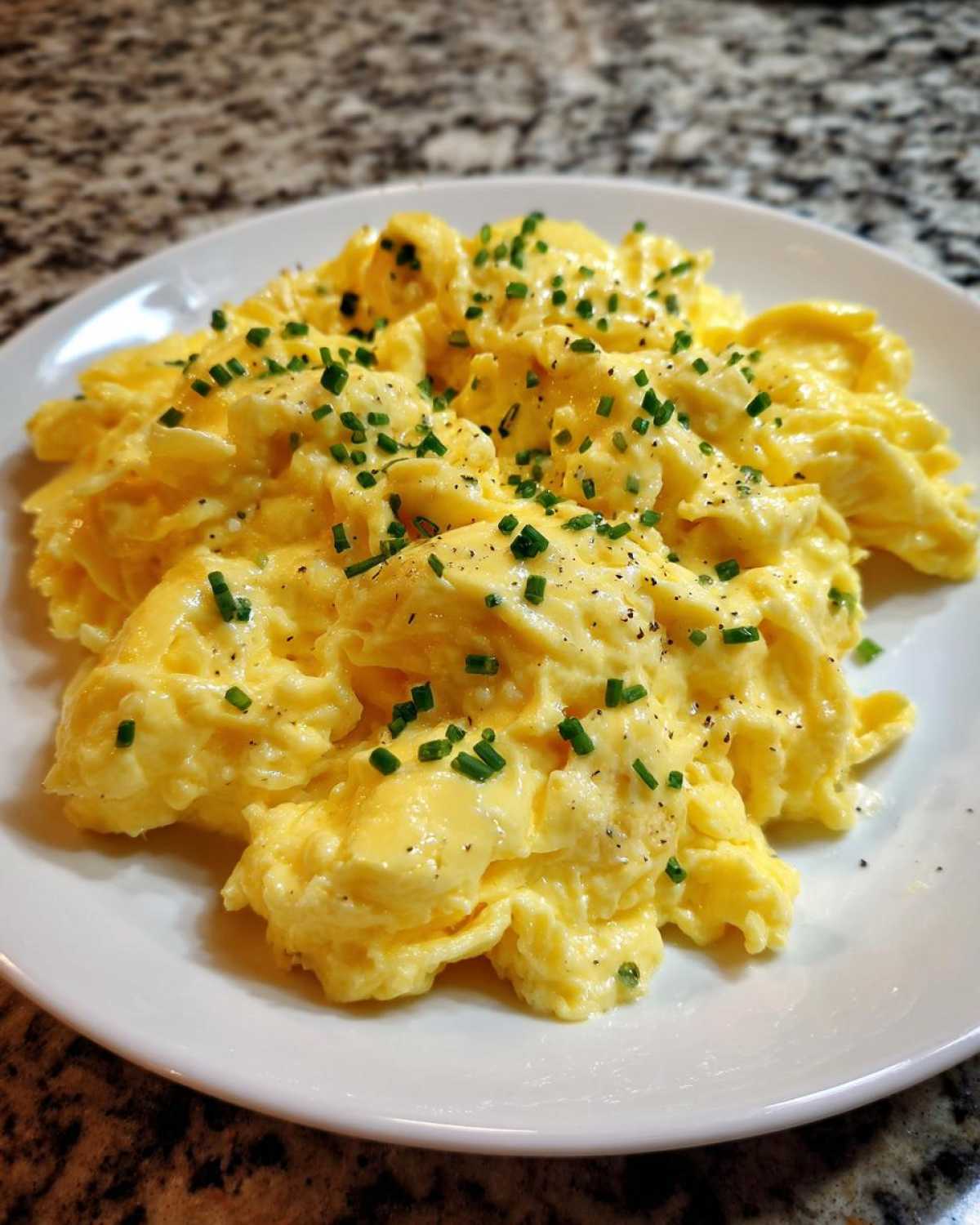 Close-up of creamy, perfectly cooked scrambled egg topped with fresh chives and black pepper.