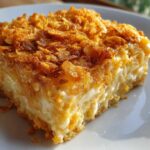 A close-up of a creamy slice of funeral potatoes recipe topped with golden brown, crispy cornflakes.