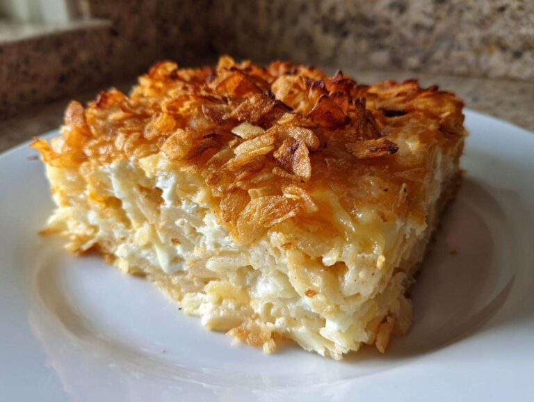 A close-up slice of creamy funeral potatoes recipe topped with golden, crispy fried onions.