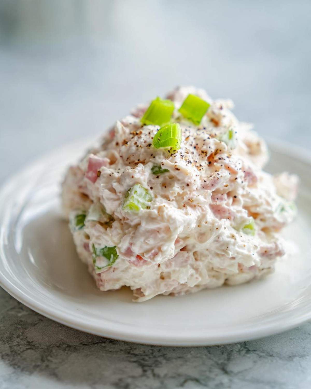 A scoop of creamy ham salad recipe mixed with celery and ham, topped with fresh green onion pieces and cracked black pepper.