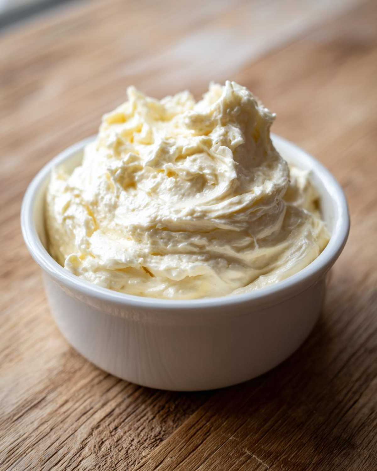 A close-up of thick, creamy Low Carb Garlic Aioli swirled high in a small white ramekin on a rustic wooden surface.