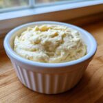 A close-up of thick, creamy Low Carb Garlic Aioli served in a small white fluted ramekin on a wooden surface.