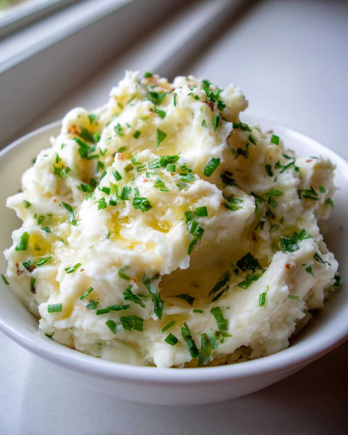 A close-up of creamy mashed potatoes topped with melted brown butter and fresh chopped chives.