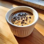Close-up of creamy peppercorn sauce topped with whole black peppercorns in a white ramekin.