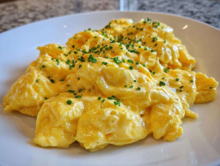 Close-up of perfectly creamy, bright yellow scrambled egg served on a white plate and garnished with fresh chopped chives.