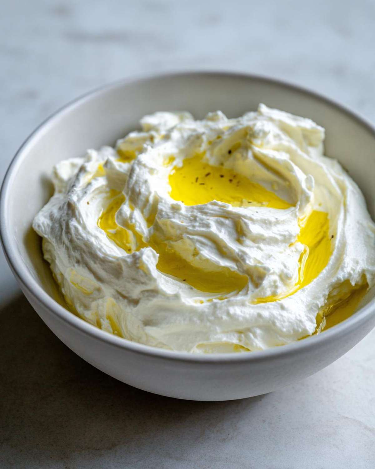 A close-up of creamy whipped feta dip topped with a pool of golden olive oil in a white bowl.