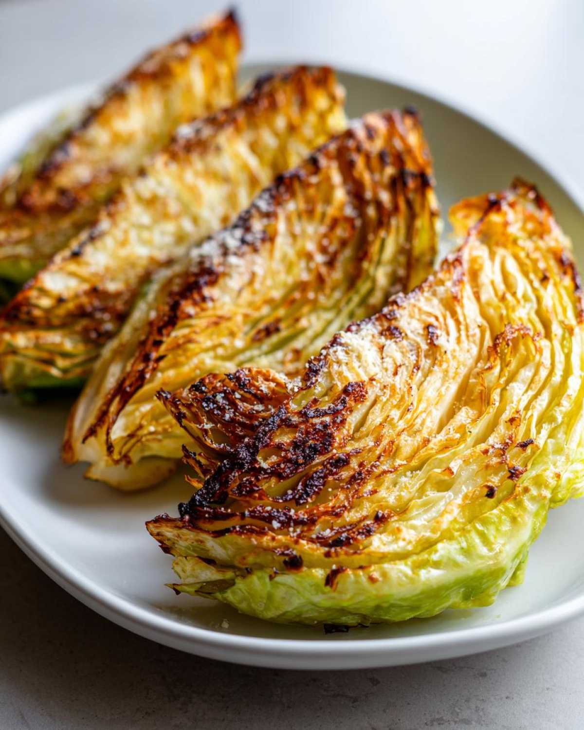 Four golden brown, crispy air fryer cabbage wedges sprinkled with seasoning on a white plate.