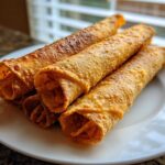 Four crispy, golden brown Chicken Taquitos stacked on a white plate, ready to eat.