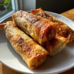 Four perfectly fried, crispy egg roll appetizers stacked on a white plate, showing golden brown, bubbly wrappers.