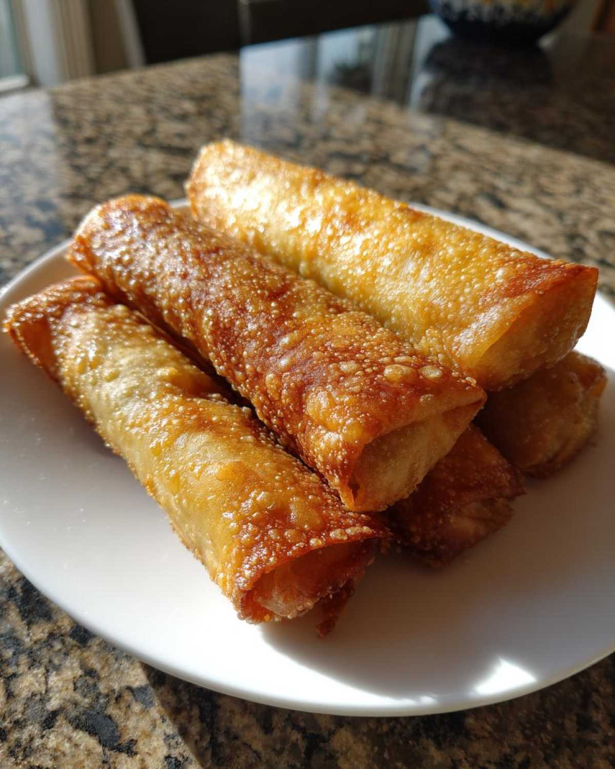 A stack of four perfectly golden brown, crispy egg roll appetizers resting on a white plate.