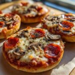 Four freshly baked english muffin pizza halves topped with melted cheese, pepperoni, and mushrooms, ready to eat.